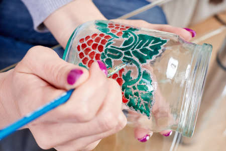 A girl paints a glass jar with stained glass paintsの写真素材