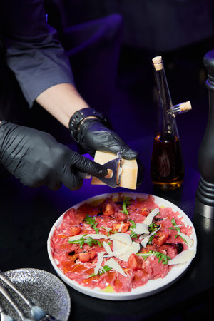 The chef prepares veal carpaccio with arugula and parmesan in front of the guests of the restaurantの写真素材