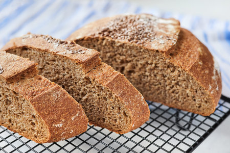 Sliced homemade round rye bread on a metal wire rack with a cloth. Close up, selective focus