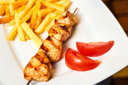 Chicken skewers with french fries and tomatoes on a white plateの写真素材