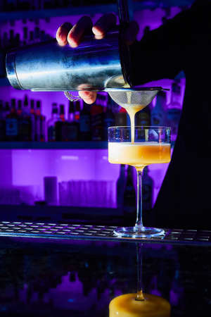 Bartender prepares Is Love alcohol cocktail on bar counter using shaker and strainerの写真素材