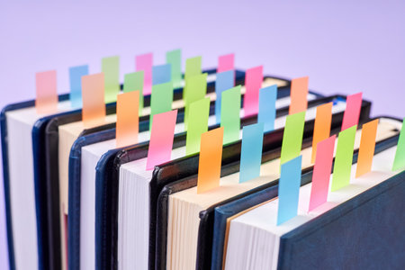 Close-up of a stack of office notepads with colorful sticky page markers sandwiched between pages on purple backgroundの写真素材