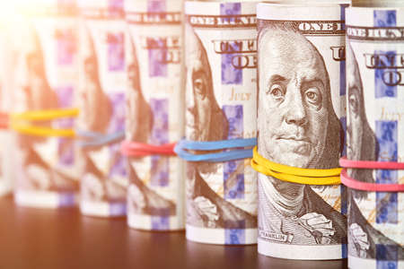 A row of rolled hundred dollar bills with rubber bands with sunlightsの写真素材