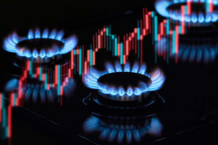 Flaming gas burners on household kitchen stove with an exchange graph of the growth in the cost of natural gas pricesの写真素材