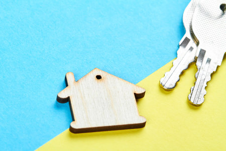 Trinket in the form of a wooden house with the keys to the apartment on the yellow-blue backgroundの写真素材