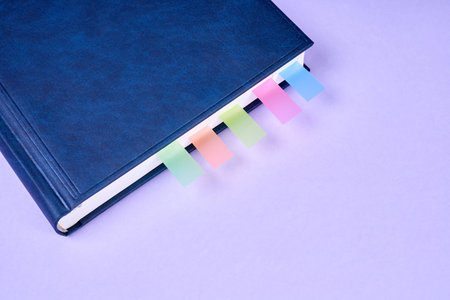 An office notepad with colorful sticky page markers sandwiched between pages on purple backgroundの写真素材