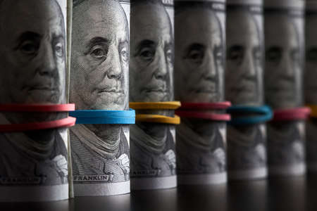 A row of rolled hundred dollar bills with rubber bands on dark backgroundの写真素材
