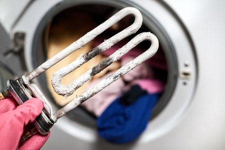 A man holds in his hand a burnt-out heating element of a washing machine against the background of a washing machineの写真素材