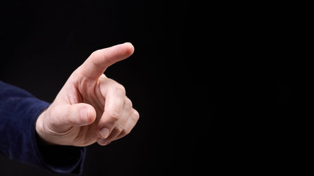 The finger of a male hand points to something on a dark background