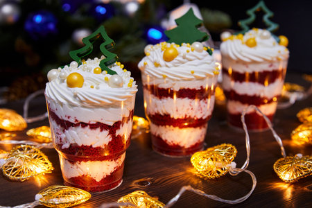 Christmas trifles in cups as a dessert, decorated with chocolate new year trees, for a festive table on a background of glowing garlandsの写真素材