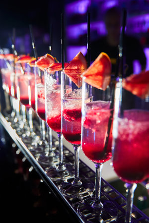 A row of glasses with champagne and grapefruit slices on the bar counter in the process of preparing...