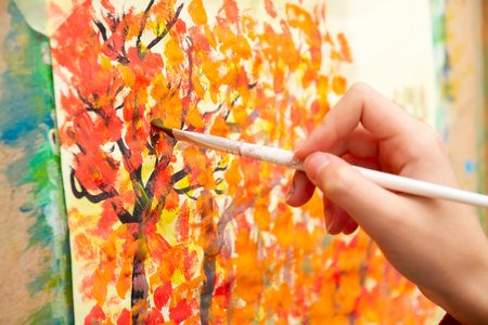 Young artist paints orange autumn trees on canvasの写真素材