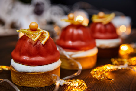 Christmas cakes made from sand tartlets, raspberry confit, and Mascarpone mousse on a background of glowing garlandsの写真素材