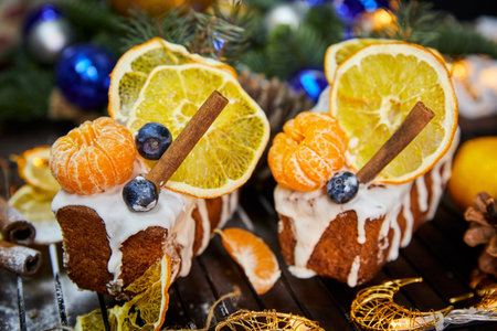 Christmas curd cake decorated with orange, tangerines, fresh blueberries on a background of glowing garlandsの写真素材