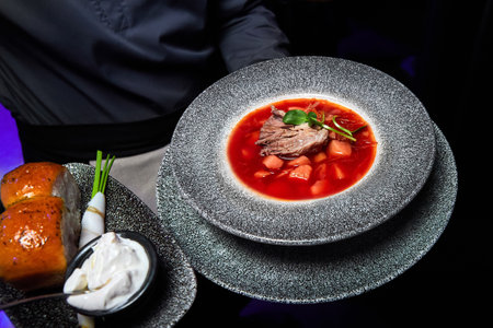 The waiter holds a plate with Borscht with veal, donuts, sour cream, onion and lardの写真素材