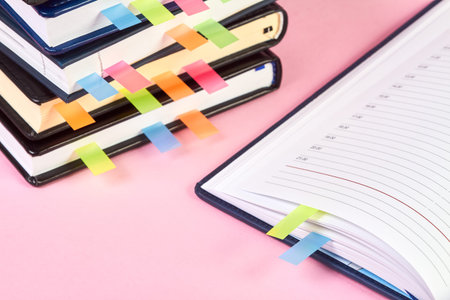 Close-up of an open notepad with colorful sticky page markers on background of a stack of office...