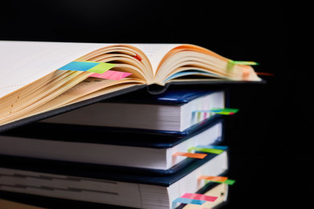 Close-up of a stack of office notepads with colorful sticky page markers with one open notepad on...