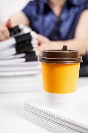 A cup of coffee on the background of an office worker sorts out a stack of papers fastened with Binder Clipsの写真素材