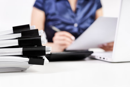 A stack of papers with Binder Clips against the background of an office worker working with documentsの写真素材