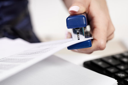 Office worker staples documents at office deskの写真素材