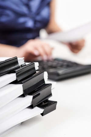 A stack of papers with Binder Clips against the background of an office worker counting on a...