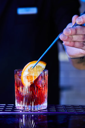 The bartender dips an orange slice into a prepared alcoholic cocktail