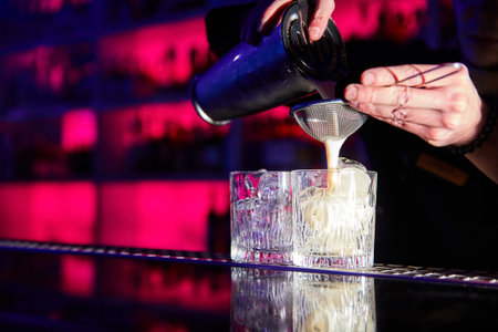 The bartender prepares cocktails on the bar counter using a shaker and a strainerの写真素材