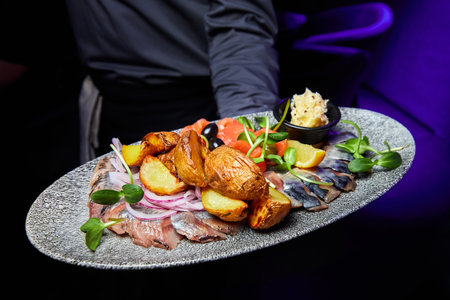 The waiter holds a plate with Atlantic Fish Plate with Onions, Baked Potato Pieces and Cream Sauce
