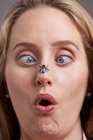 Surprised woman looking cross-eyed at a fly on her nose - focus on fly