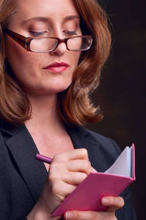 Businesswoman with glasses wriring in pink notebookの写真素材