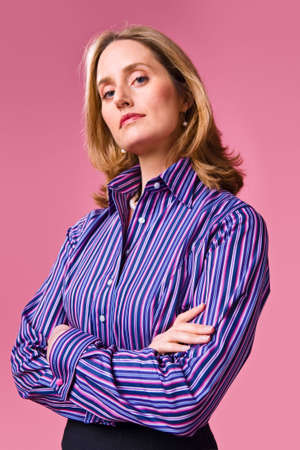 Businesswoman with arms folded wearing striped shirt on a pink backgroundの写真素材