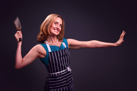 Glamorous housewife wearing butcher's apron and holding meat cleaver の写真素材