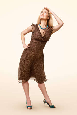 Full-length portrait of classic model wearing brown dress and looking up on pale backgroundの写真素材