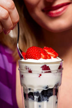 Close-up of woman eating a mixed berry yoghurt parfait -- focus on dessertの写真素材