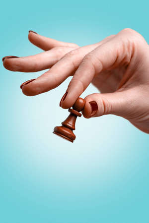 Woman's hand holding chess pawn on blue backgroundの写真素材