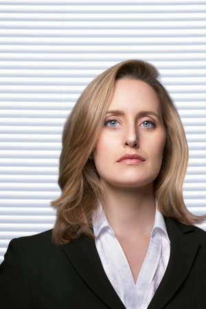 Portrait of female detective with serious facial expression infront of white slatted blindsの写真素材