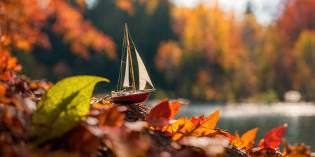 Toy sailboat on the bank of a lake surrounded by autumn leavesの素材