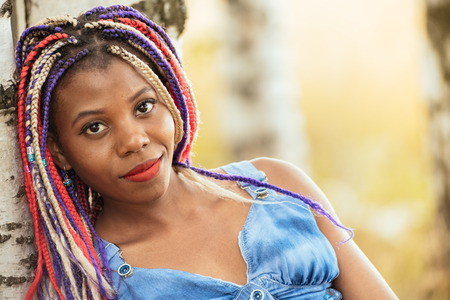 portrait of a beautiful young African American girl with a dreddy hairdress on a park background, nature, deciduous forest, photo walk concept in the fresh airの写真素材
