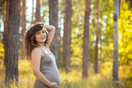 portrait of a beautiful young pregnant girl in a trendy dress against the background of an autumn forestの写真素材