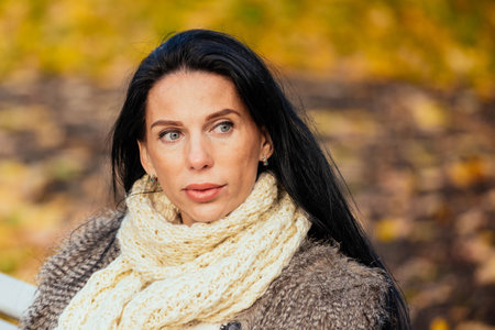 portrait of a beautiful young girl sitting on a bench in an autumn parkの写真素材
