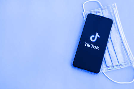 Tver, Russia - September 19, 2020: Tiktok app on the smartphone screen and medical protective mask on a blue background. TikTok is a popular video sharing social network owned by ByteDance.のeditorial素材