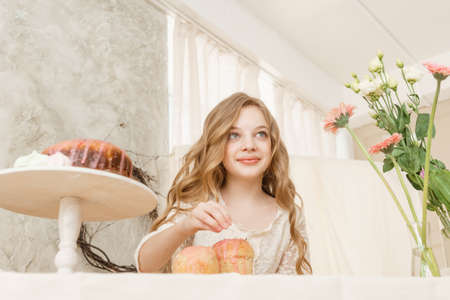 A girl with long hair in a light dress is sitting at the Easter table with cakes, spring flowers and quail eggs. Happy Easter celebration.の写真素材