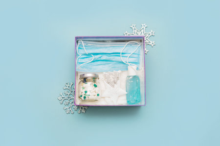 Medical mask, pills in a jar, antiseptic gel for hands and Christmas decorations in a box on a blue...