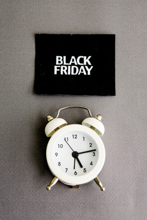 white alarm clock and an inscription on a black square - black Friday on a gray background. The...