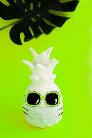 Pineapple in a medical mask and sunglasses on green neon background. Summer in . Vision for the...