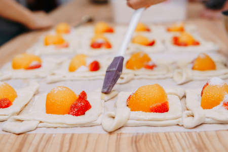 Preparing a dessert at a cooking master class. Baskets with peaches and strawberries, home cooking. Close-up, selective focus. Pastries, pies with peaches from puff pastry.の写真素材