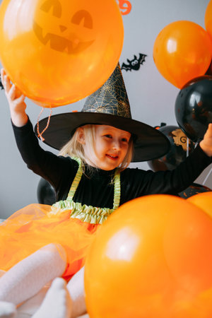 Childrens Halloween - a girl in a witch hat and a carnival costume with airy orange and black balloons at home. Ready to celebrate Halloween.の写真素材