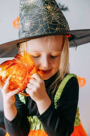 Childrens Halloween - a girl in a witch hat and a carnival costume with airy orange and black balloons at home. Ready to celebrate Halloween.の写真素材