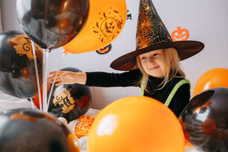 Childrens Halloween - a girl in a witch hat and a carnival costume with airy orange and black balloons at home. Ready to celebrate Halloween.の写真素材