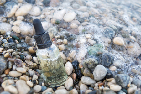 Cosmetic serum in a glass bottle with a pipette on stones